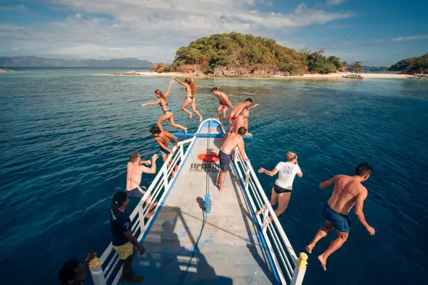 Group of travelers jumping off the Seatours expedition boat bow into turquoise tropical water during a private 3D2N Palawan expedition charter